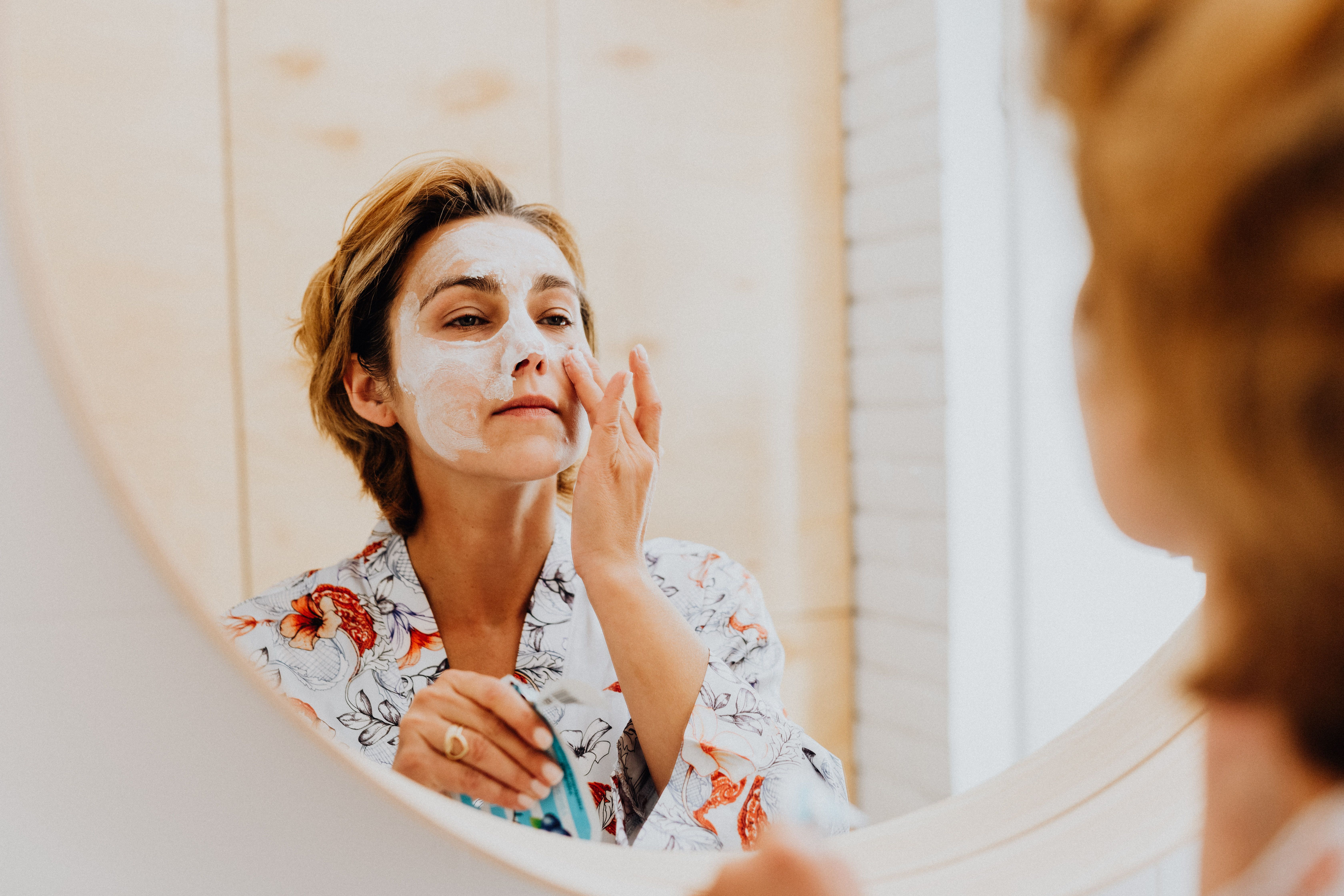 Woman looking in a mirror completing her skincare beauty routine.
